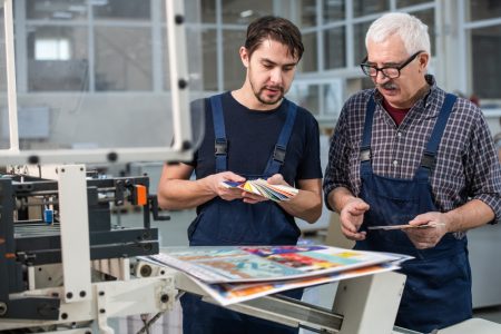 Busy,Printing,Plant,Workers,Standing,At,Printed,Pages,And,Choosing